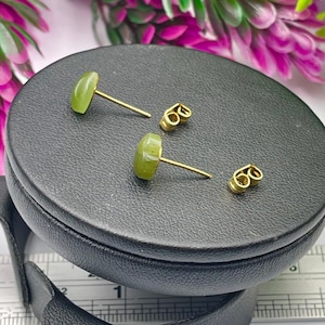 Puede incluir: Un par de pendientes de piedra verde con postes de oro y cierres de mariposa. Los pendientes se muestran en una caja de terciopelo negro.