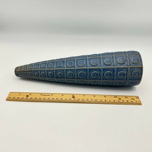 Può includere: Un vaso in ceramica blu con un motivo geometrico di cerchi e quadrati. Il vaso è a forma di cono e misura circa 30 cm di lunghezza.