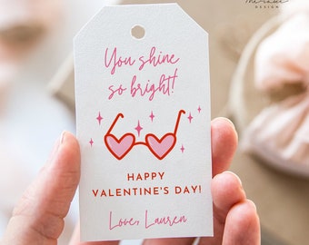 May include: A white gift tag with pink and red heart-shaped sunglasses and the text "You shine so bright! Happy Valentine's Day! Love, Lauren".
