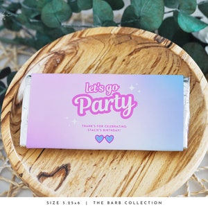 May include: A pink and blue gradient chocolate bar wrapper with the text "let's go Party" in pink and white lettering. The wrapper also includes the text "THANK'S FOR CELEBRATING STACIE'S BIRTHDAY!" with two blue hearts. The wrapper is 5.25 inches by 6 inches.
