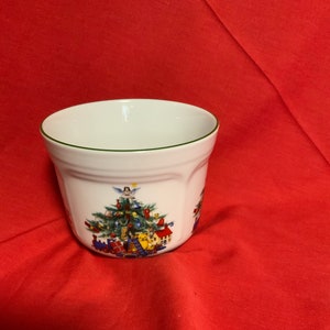 May include: White ceramic Christmas themed planter with a green rim. The planter features a Christmas tree with ornaments, presents, and a toy train.