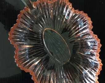 May include: A pink glass leaf-shaped dish with a scalloped edge and a handle. The dish is clear and has a ribbed design.