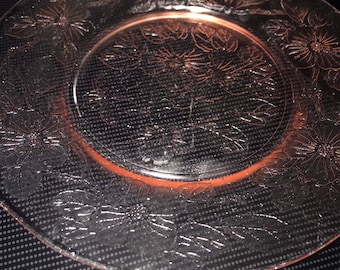 May include: A clear glass plate with a floral design. The plate has a raised rim and a center well. The floral design is etched into the glass and features a repeating pattern of flowers and leaves.