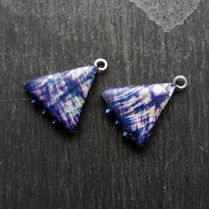 May include: Two triangle-shaped pendants with a blue and white tie-dye pattern and silver jump rings. Each pendant has a row of blue beads.