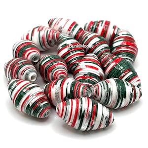 May include: A collection of barrel-shaped beads featuring a striped pattern in red, dark green, white, and silver. Each bead has a central hole and a glossy finish. The text BunkiMoose is visible in the center of the bead arrangement.