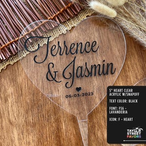 May include: A clear acrylic heart-shaped wedding cake topper with the names "Terrence & Jasmin" and the date "06-03-2023" in black script. The topper is 5 inches in size and has a snap-off design.