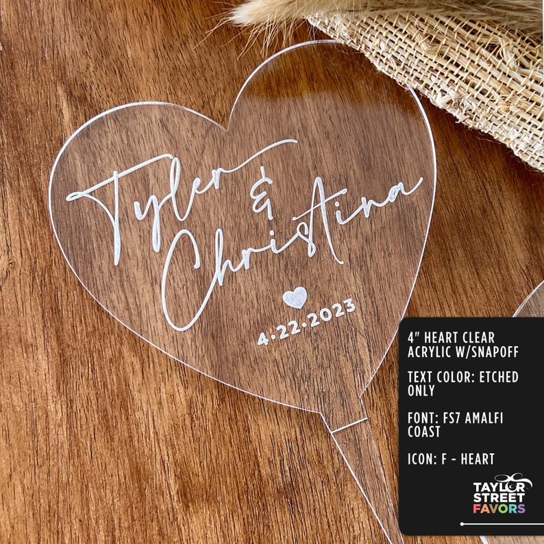 May include: A clear acrylic heart-shaped wedding favor with the names "Tyler & Christina" and the date "4.22.2023" etched in white. The favor is 4 inches in size and has a snap-off feature.
