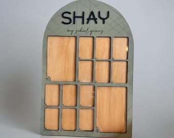 May include: An arched wooden school years photo board with a sage green finish and black text reading SHAY and my school years. The board features one large rectangular slot, several smaller photo slots, and labels for grades PK through 12.