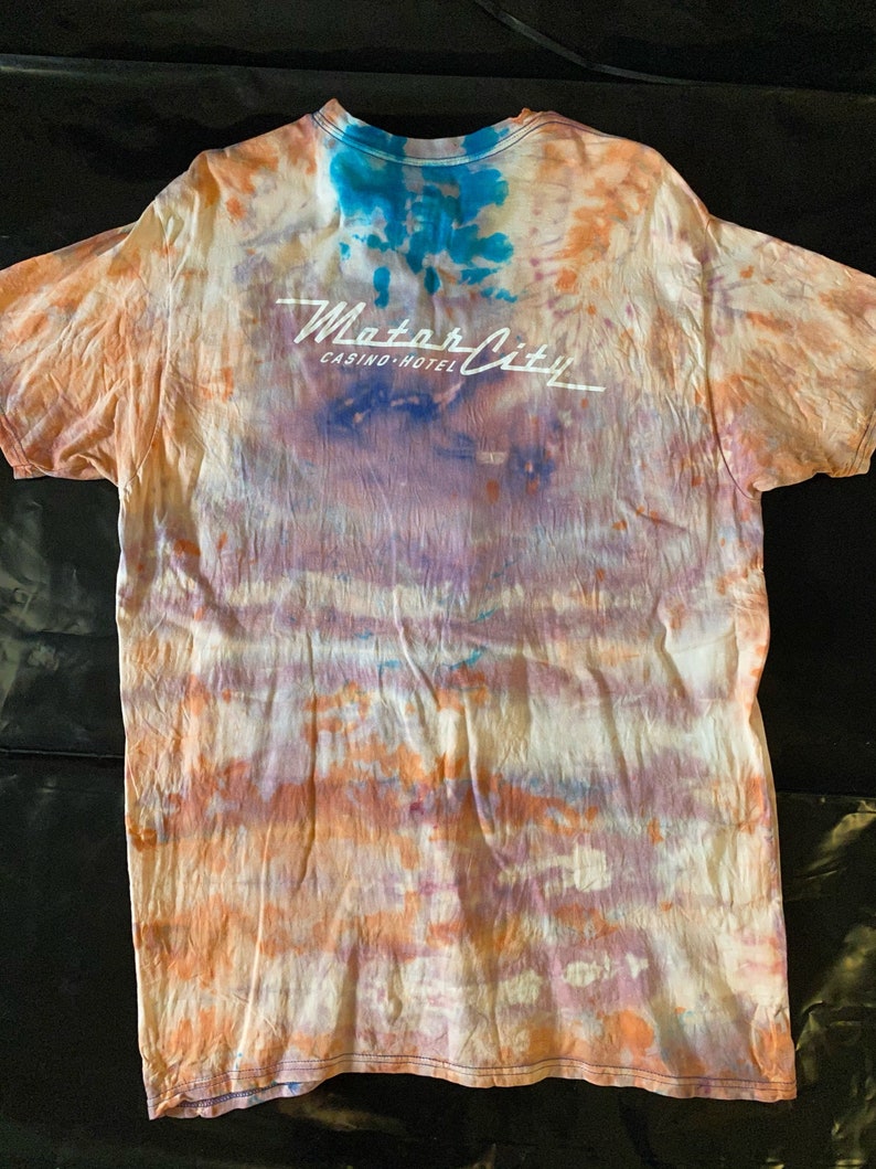 May include: A tie-dye t-shirt with an orange, blue, and purple color scheme. The shirt has the text "Motor City Casino-Hotel" printed on the back.