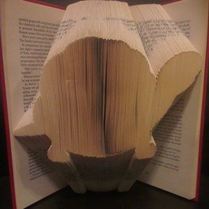May include: A book folded into the shape of a bird. The book is open and the pages are folded to create the shape of the bird. The book is on a black surface.