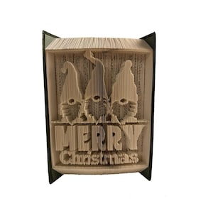 Peut inclure: Une sculpture d'art de livre avec trois gnomes et les mots "Joyeux Noël" pliés dans les pages. Le livre est relié en vert.