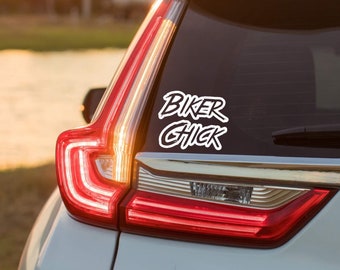 May include: A white vinyl decal applied to the rear window of a vehicle. The decal features the text BIKER CHICK in a bold, stylized, hand-lettered font. The letters are white with a clean, sharp outline, contrasting against the dark glass surface.