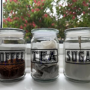 May include: Three glass jars with black labels and white text. The labels read "Coffee", "Tea", and "Sugar".