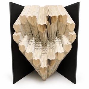 Könnte beinhalten: Ein Buch mit gefalteten Seiten, die eine Herzform bilden, mit mehreren herzförmigen Ausschnitten in der gesamten Struktur. Das Buch hat einen einfarbigen schwarzen Einband, der offen steht und einen starken Kontrast zu den cremefarbenen Seiten bildet.
