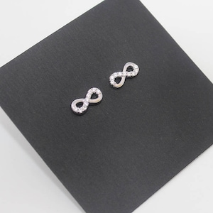 May include: A pair of silver infinity symbol earrings with small clear cubic zirconia stones.