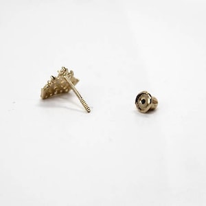 May include: A pair of gold earrings with a geometric design. The earrings are small and delicate, and they have a simple, elegant style.