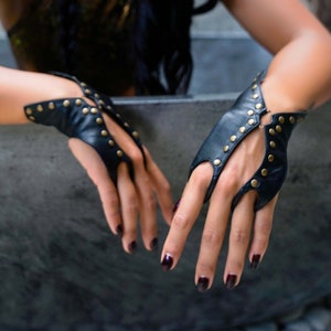 Soft black leather hand bracelet embellished with metal studs and wrist metal buttons to fasten. Black fingerless gloves, festival wear punk, emo, and rock n roll style accessories.
