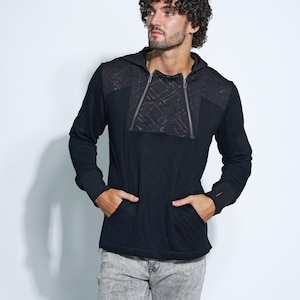 May include: A black hooded sweatshirt with a zippered front and a quilted panel on the chest. The sweatshirt has long sleeves and pockets on the sides. The model is wearing grey jeans.