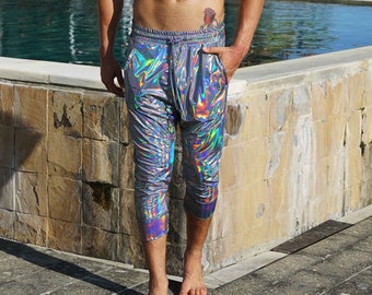Könnte beinhalten: Ein Mann trägt eine silberne, schimmernde Hose mit einem Kordelzug. Er steht an einem Pool und hat ein Tattoo auf der Hüfte.