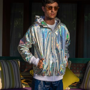 Silver waterproof holographic windbreaker for men. A loose-fit rave jacket with white thumbhole cuffs, full-zip front, and hood by Love Khaos