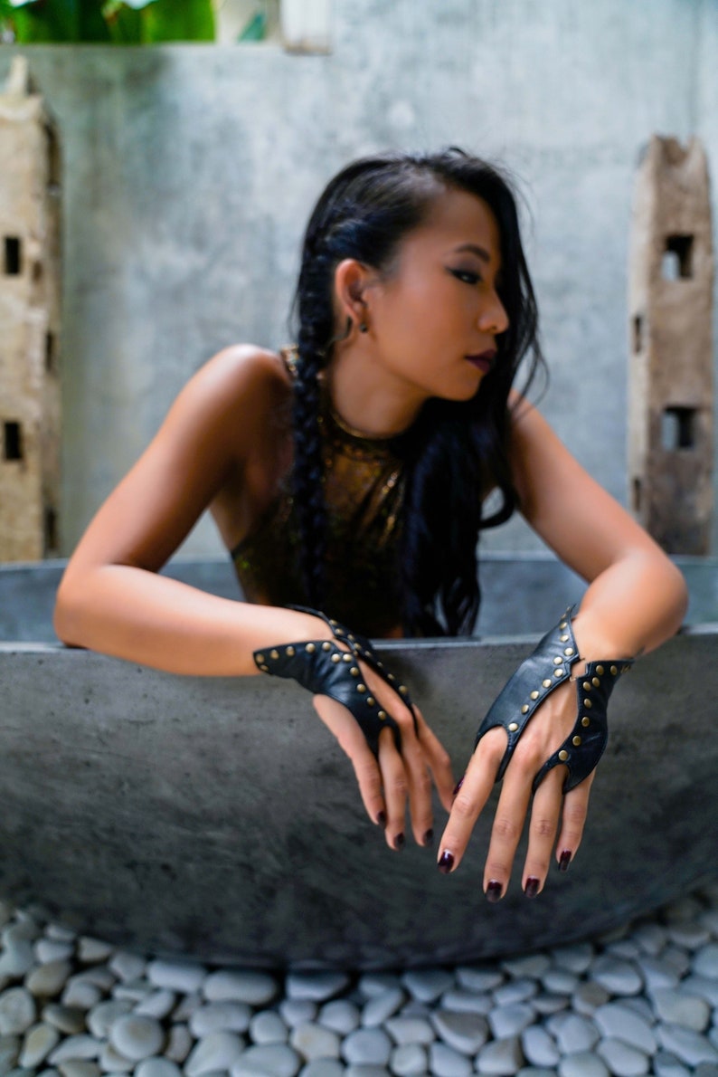 Soft black leather hand bracelet embellished with metal studs and wrist metal buttons to fasten. Black fingerless gloves, festival wear punk, emo, and rock n roll style accessories.