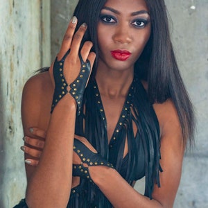 Soft black leather hand bracelet embellished with metal studs and wrist metal buttons to fasten. Black fingerless gloves, festival wear punk, emo, and rock n roll style accessories.