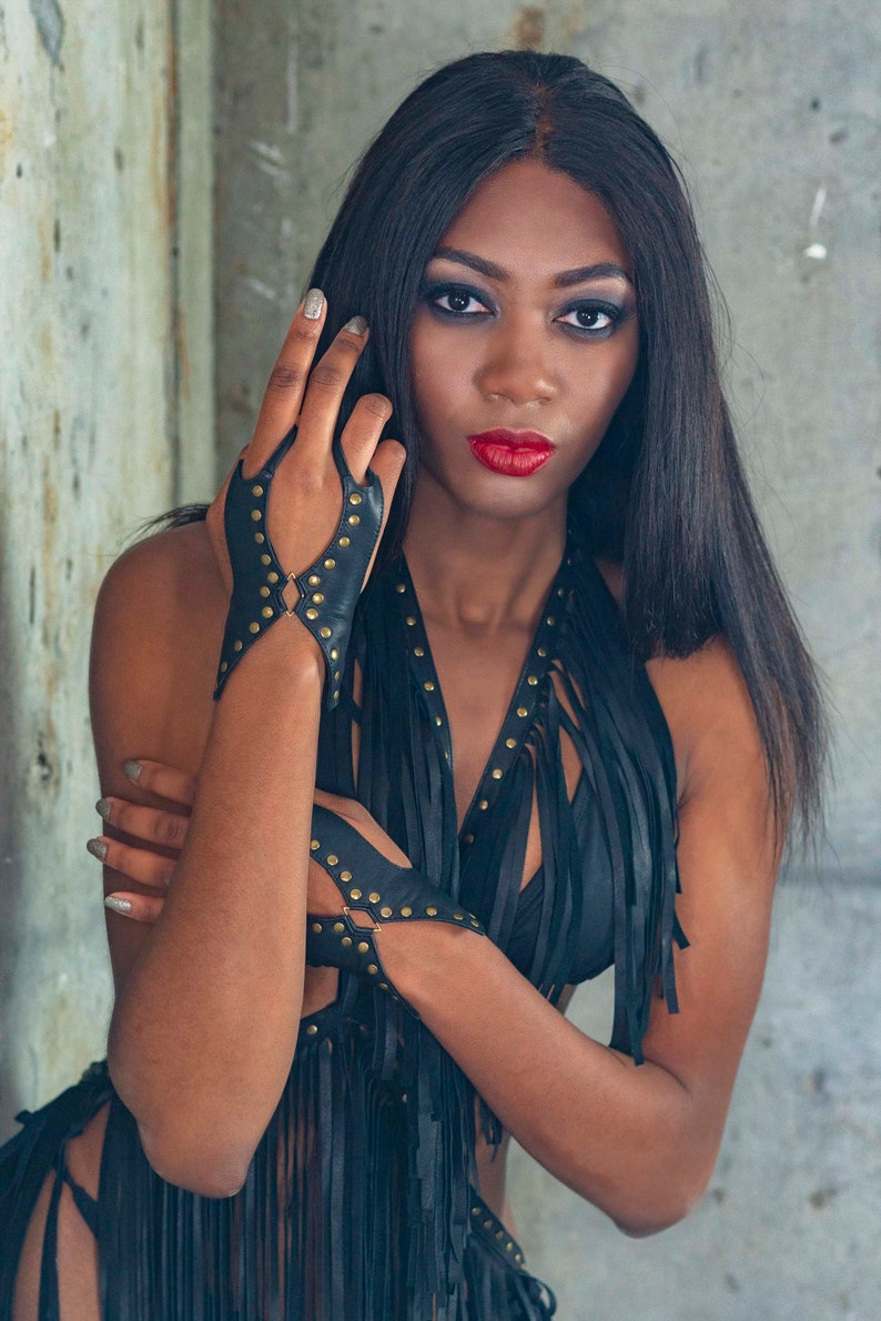 Soft black leather hand bracelet embellished with metal studs and wrist metal buttons to fasten. Black fingerless gloves, festival wear punk, emo, and rock n roll style accessories.