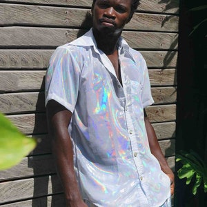 Puede incluir: Una camisa blanca iridiscente con botones y mangas cortas y unos pantalones cortos plateados iridiscentes con un patrón azul y morado.