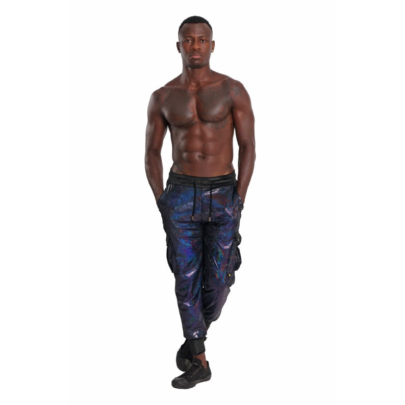 May include: A man wearing black cargo pants with a iridescent blue and purple pattern. The pants have a drawstring waist and cargo pockets.