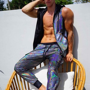 May include: A man wearing a black and iridescent sleeveless hoodie and iridescent pants. He is sitting on a bamboo chair with a white cushion.