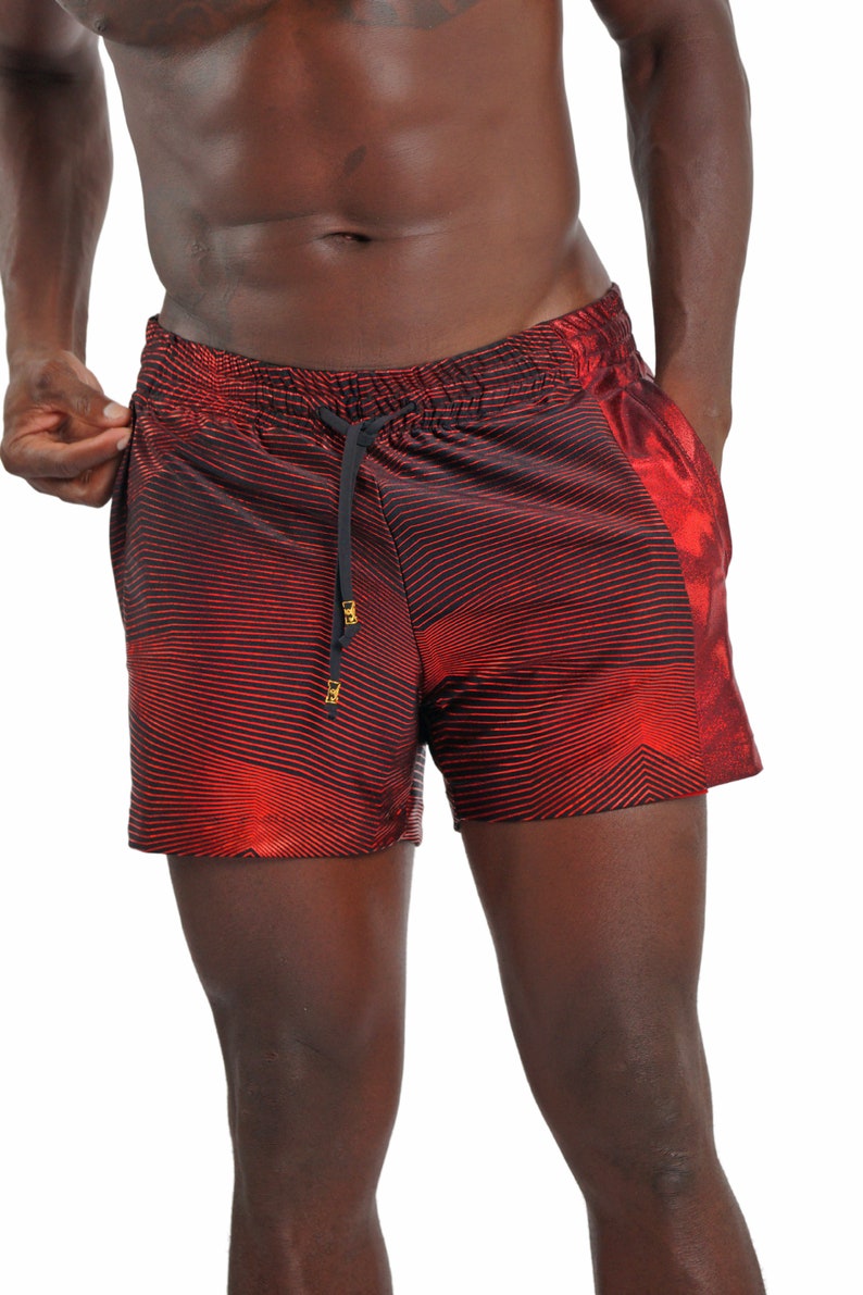 May include: Red and black striped swim trunks with a gold drawstring. The trunks have a wavy pattern.