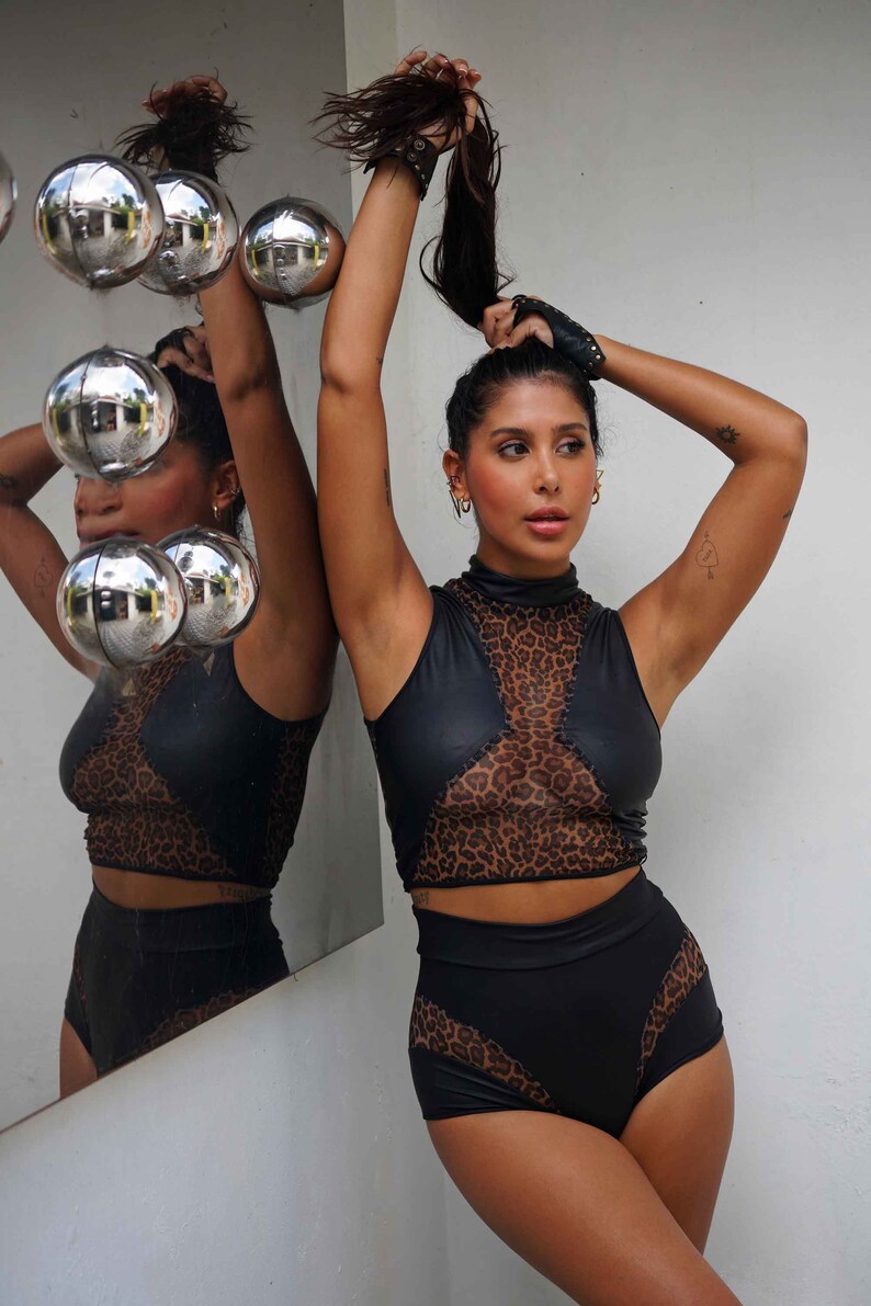 Peut inclure: Une femme portant un haut court noir et marron &agrave; imprim&eacute; l&eacute;opard avec un panneau en mesh et un short taille haute assorti.