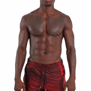 May include: A man wearing red and black striped swim trunks with a drawstring waist.