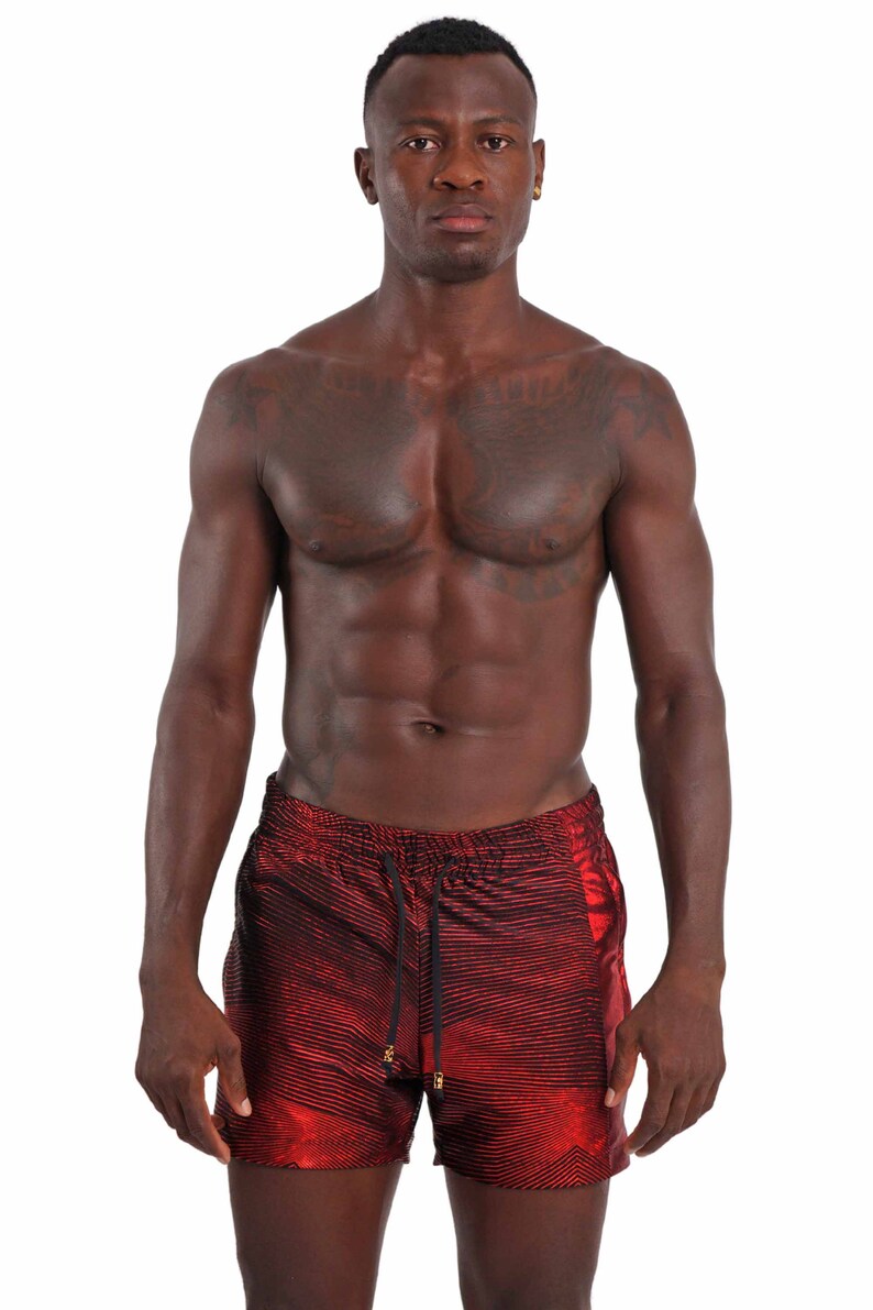 May include: A man wearing red and black striped swim trunks with a drawstring waist.