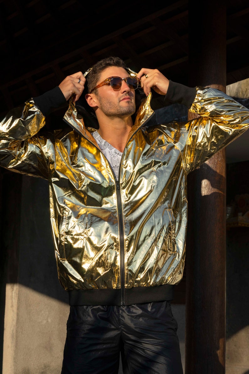 Metallic gold windbreaker for men, with black thumbhole cuffs, full-zip front, and hood by Love Khaos