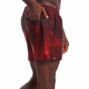 May include: Red and black patterned swim trunks with a zippered pocket on the side.