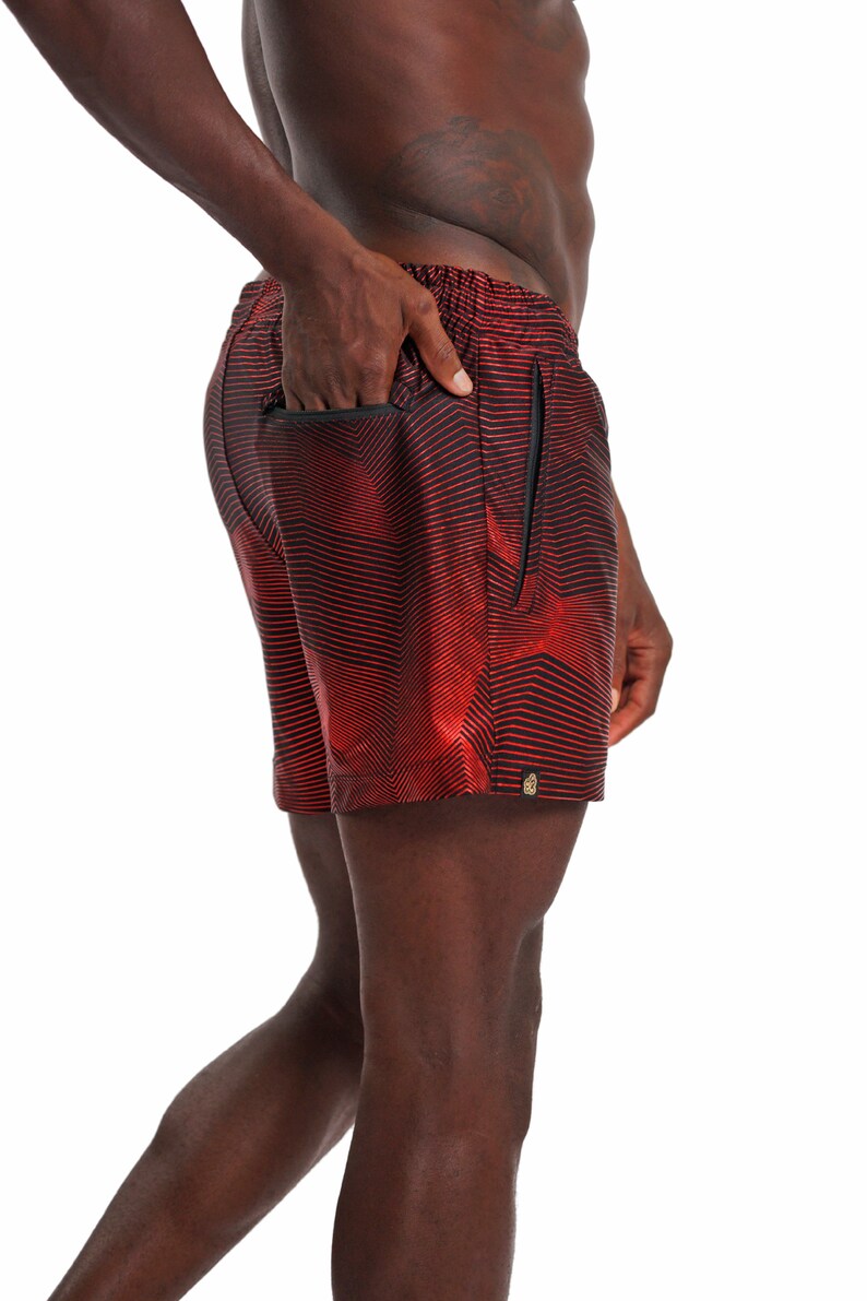 May include: Red and black patterned swim trunks with a zippered pocket on the side.