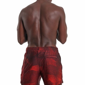 May include: A man wearing red and black patterned swim trunks. The trunks have a geometric design.