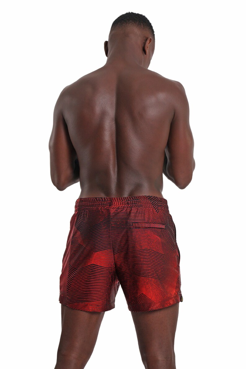 May include: A man wearing red and black patterned swim trunks. The trunks have a geometric design.