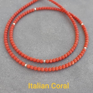 Puede incluir: Dos collares de cuentas de coral rojo con pequeñas cuentas plateadas. Los collares se muestran sobre una superficie gris. El texto "Italian Coral" está en la parte inferior.