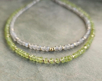 May include: A layered necklace set featuring one strand of faceted light green peridot beads and one strand of faceted translucent gray labradorite beads, both accented with small, round, polished gold-tone metal spacer beads.