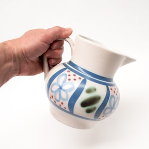 May include: A white ceramic jug with a blue and green floral design. The jug has a handle and a spout.