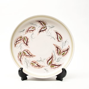 May include: A white ceramic plate with a brown and green paisley design. The plate is on a black stand.
