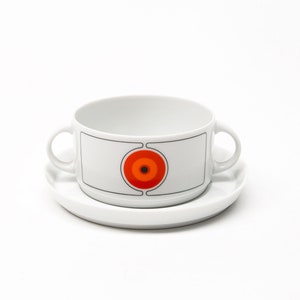 May include: White ceramic soup bowl with two handles and a saucer. The bowl features a geometric design with a red, orange and black circle in the centre.