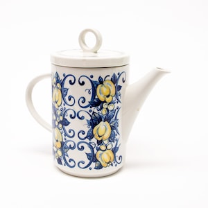 May include: A white ceramic teapot with a blue and yellow floral design. The teapot has a lid with a small handle and a spout.