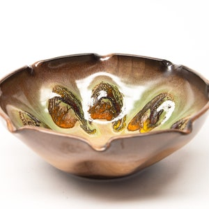 May include: A ceramic bowl with an unusual, organic form. The outside is a warm brown, and the inside has a mix of green, orange, and white details. The rim has a gently scalloped edge, adding to its artistic appeal.