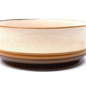 以下が含まれることがあります： ベージュの斑点模様のインテリアと茶色の外観のセラミックボウル。ボウルは、丸みを帯びた縁と濃い茶色のベースを備えた、幅が広く浅い形状をしています。ボウルはおそらく食べ物の提供に使用されます。