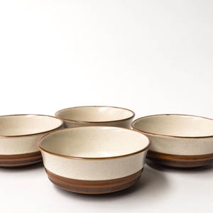 以下が含まれることがあります： クリーム色の内側とベース周りの茶色の帯が特徴の、4つのセラミックボウル。縁も茶色です。ボウルは白い背景にグループで配置されています。これらのボウルは、スープ、シリアル、または軽食の提供に適しています。