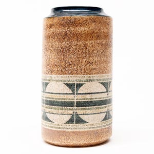 以下が含まれることがあります： テクスチャ加工された茶色の表面と濃い青色の縁を持つ円筒形のセラミック花瓶。花瓶には、白、緑、黒の幾何学模様の帯があります。装飾品です。