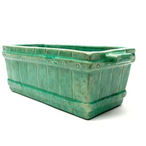 May include: A rectangular ceramic planter with a vibrant turquoise green glaze. The exterior features a moulded vertical slat design with horizontal bands and small circular details along the top and bottom edges, finished with integrated side handles.